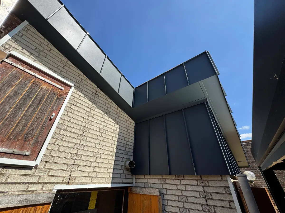 Anbau mit dunkler Metallverkleidung an einer hellen Klinkerwand, von unten gegen den Himmel fotografiert